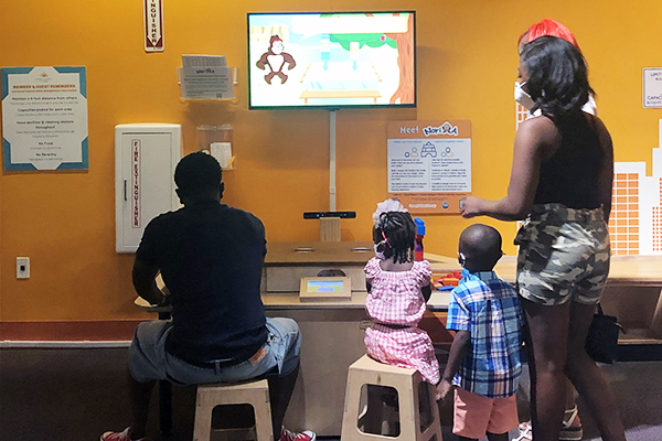  A family sits and stands in front of a an exhibit in a museum exhibit.