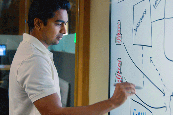  A man in a white polo shirt sketches on a dry erase board.