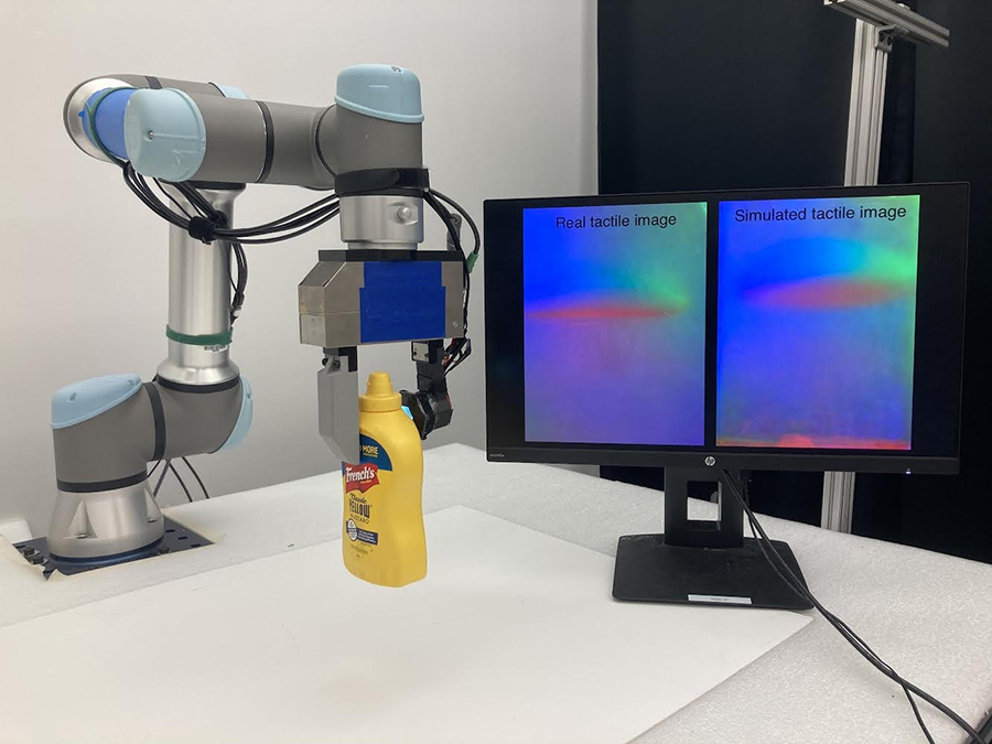  A robotic arm on the left of the sceen grasps a yellow mustard bottle in a claw-like hand while a nearby computer monitor shows how the robot's performance compares to a simulation of the same task.