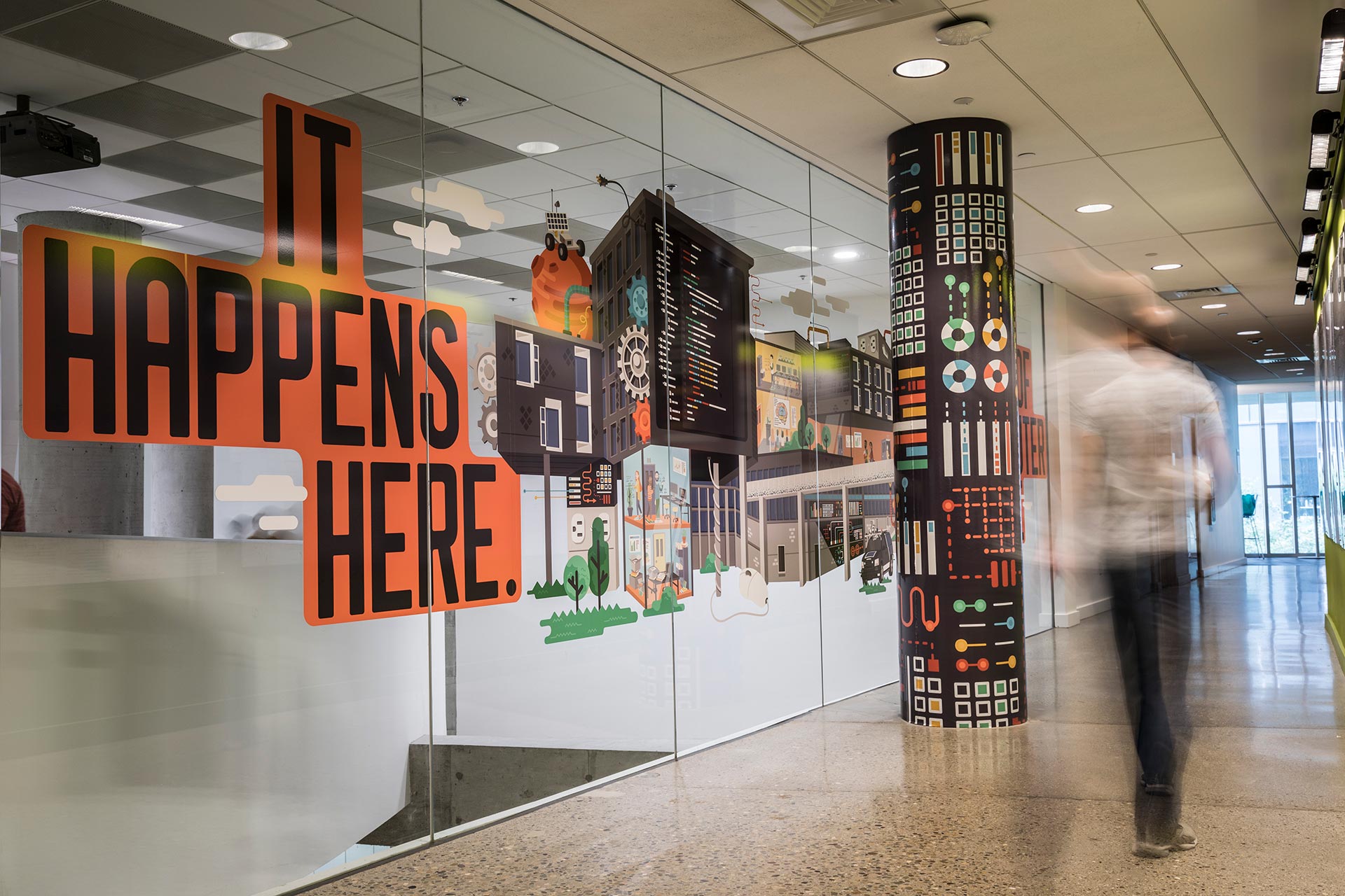 A person walks past a large mural depicting the Gates Hillman center, with the text It Happens Here.